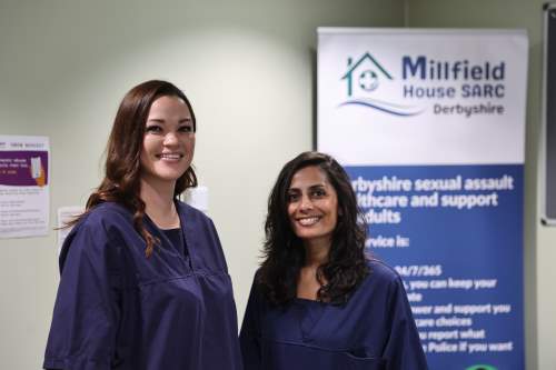 Katie and Nishali from SARC standing side by side in front of banner, smiling