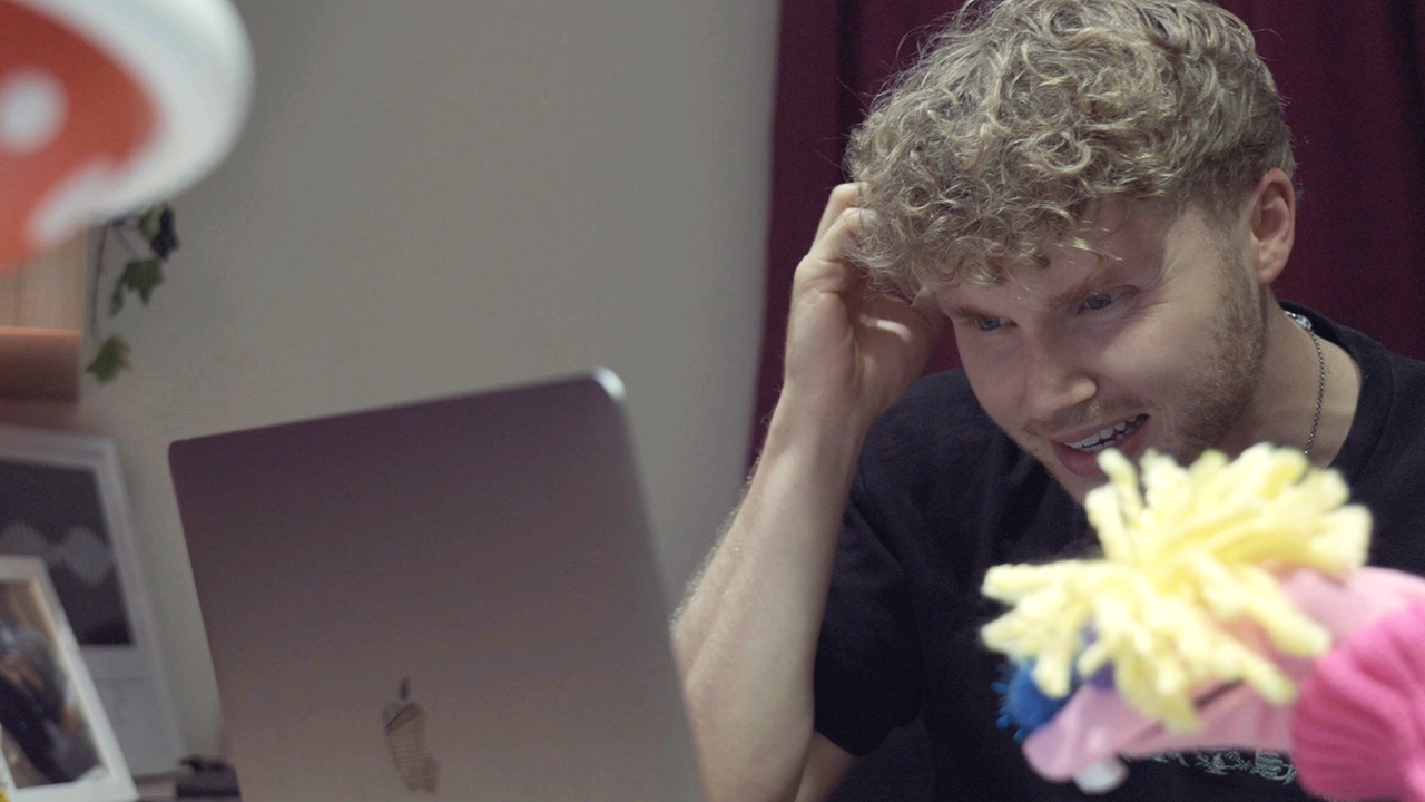 Claude the bright pink sock puppet and a young student called Connor look at a laptop screen.