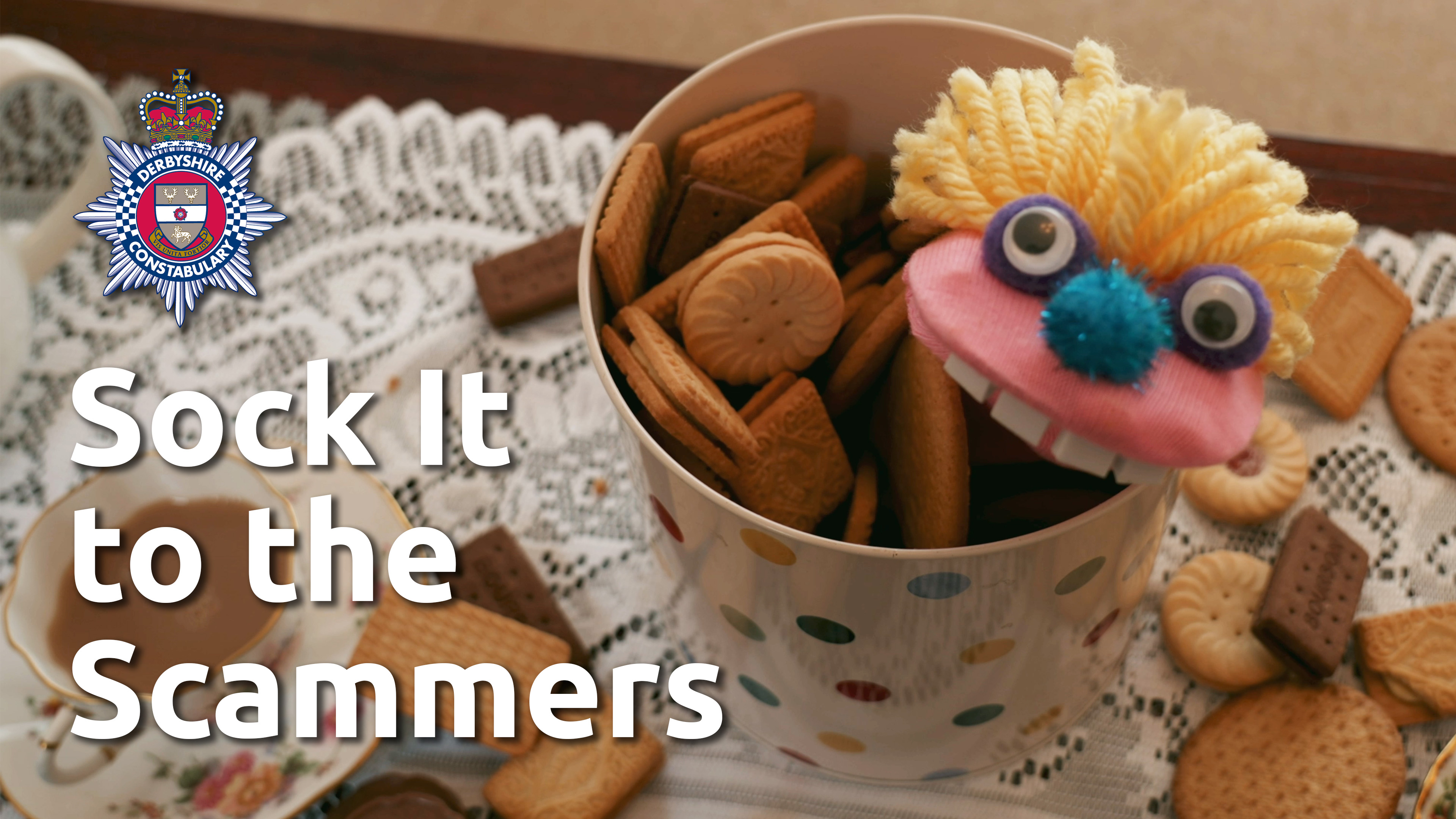 Sock It to the Scammers title card, with Claude the pink puppet emerging from a biscuit barrel.