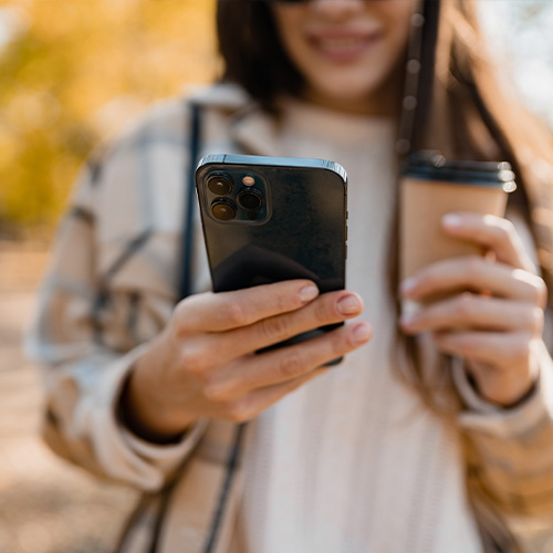 A student holds a cup of coffee and looks at their phone.