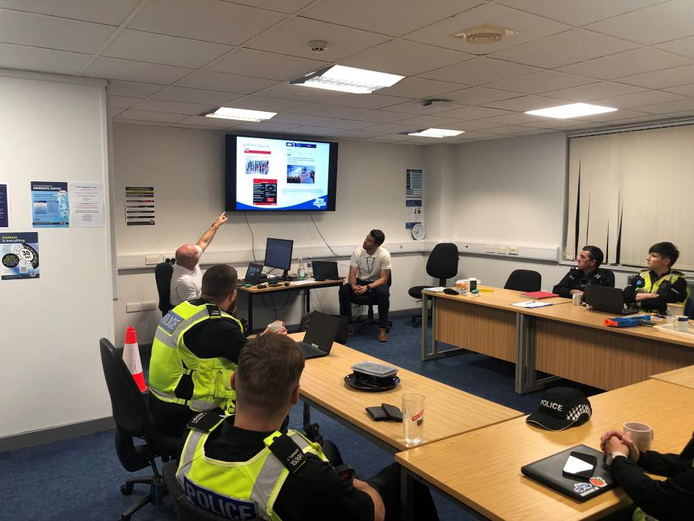 Officers around a table in a room, looking at a screen, training on how to use naloxone