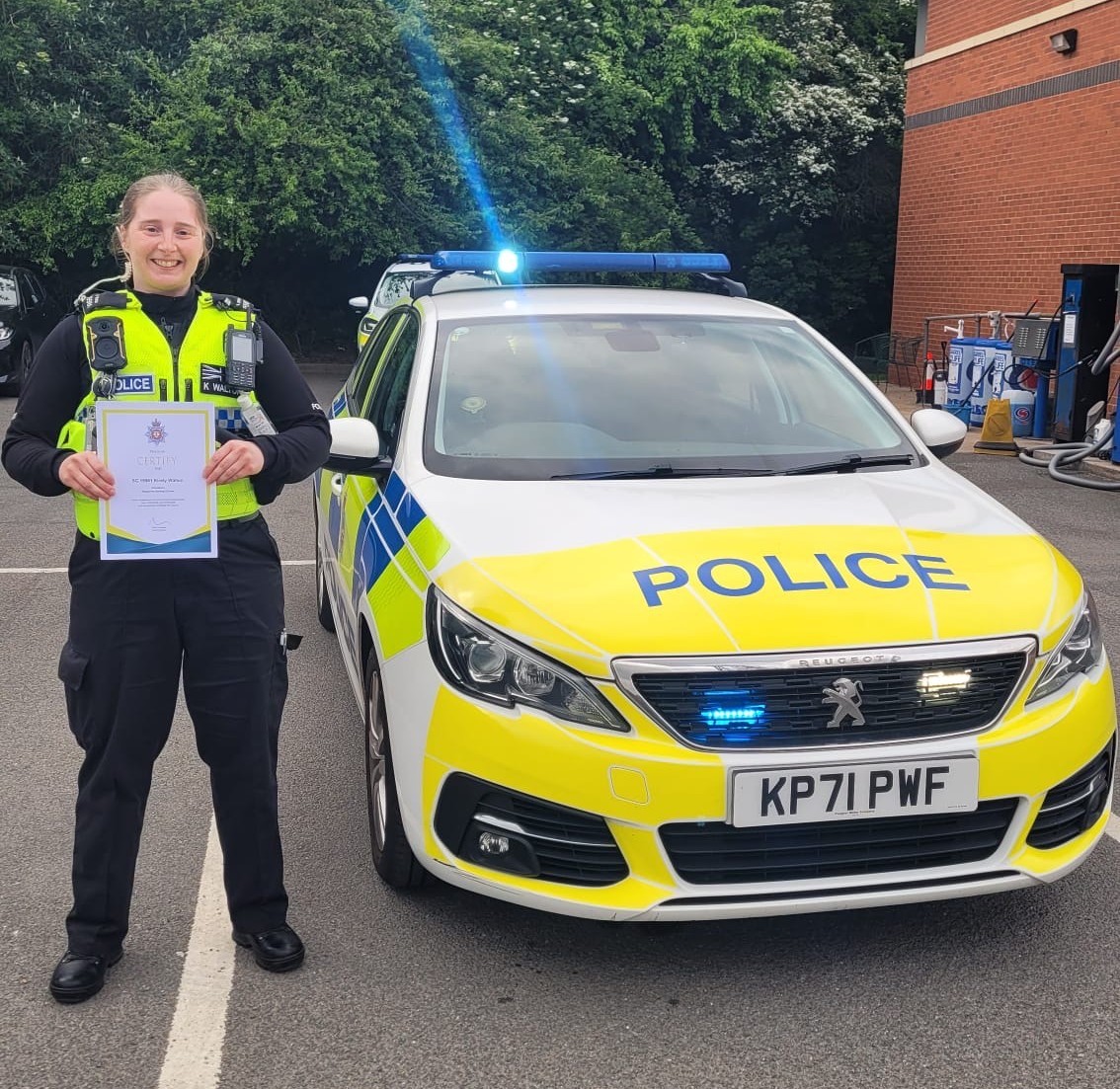 SC Walton stands by a marked police car smiling and holding a certificate.