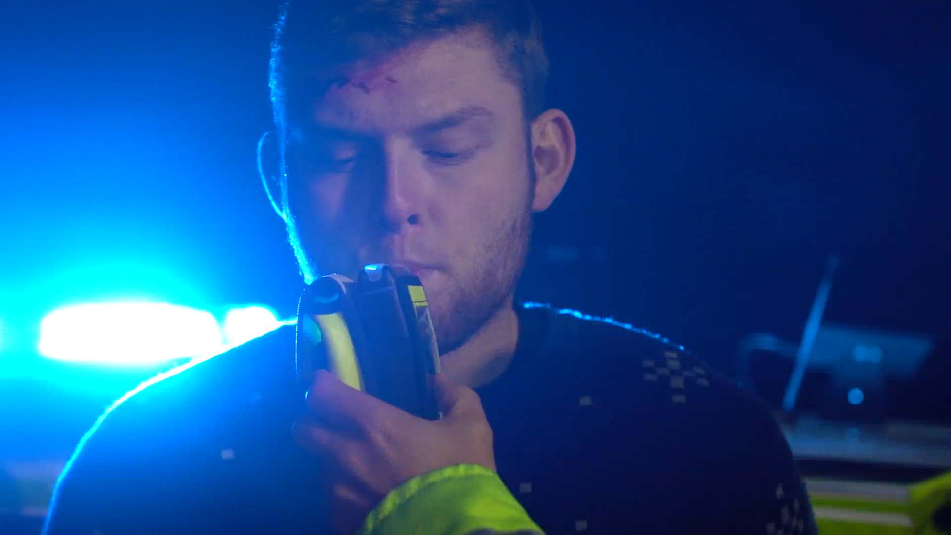 An image of a male with cuts and bruises to his face blowing into a police breathalyser. 