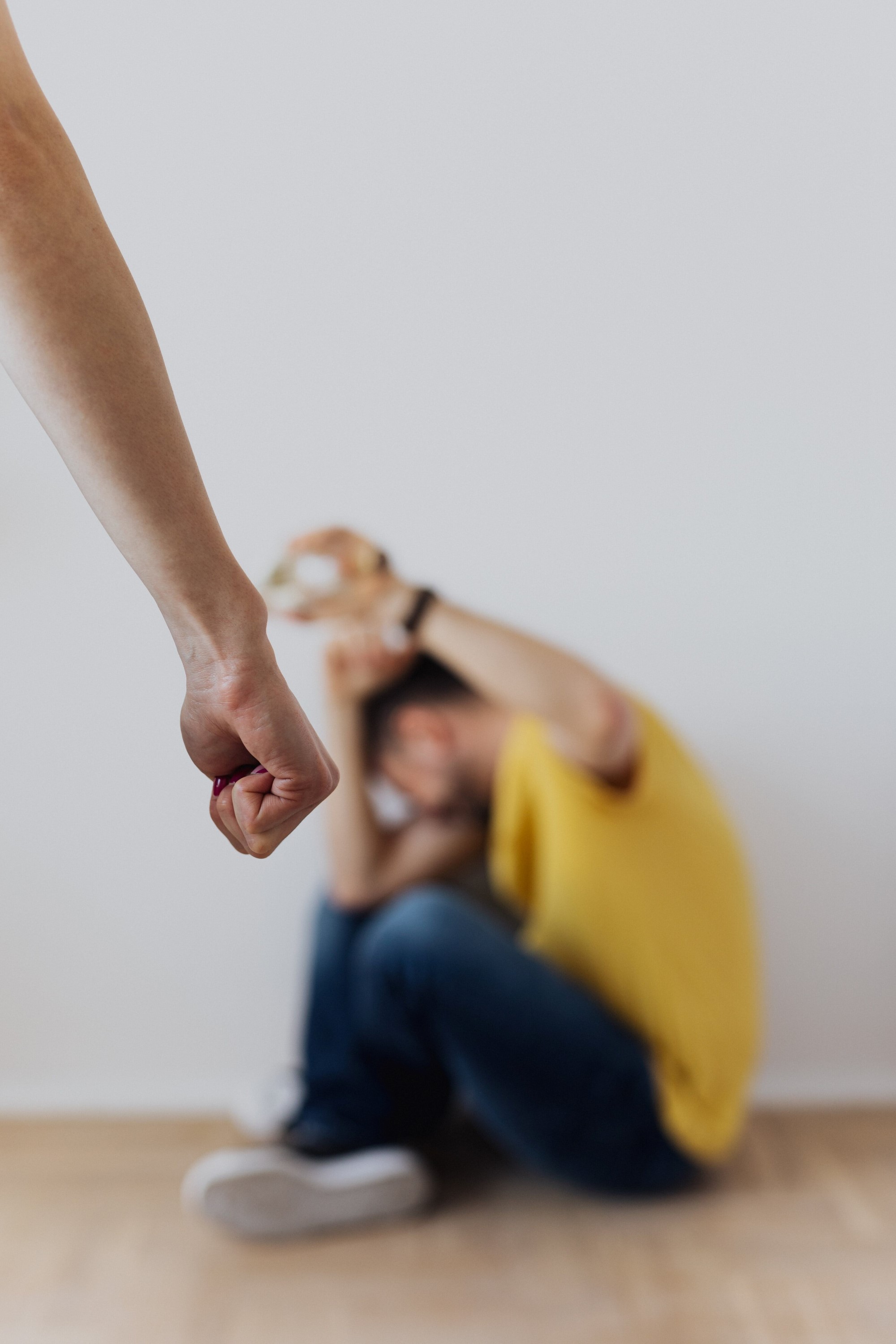 Stock image of a man sat on the floor holding his arm up to protect himself while someone stands in front of him with a clenched fist