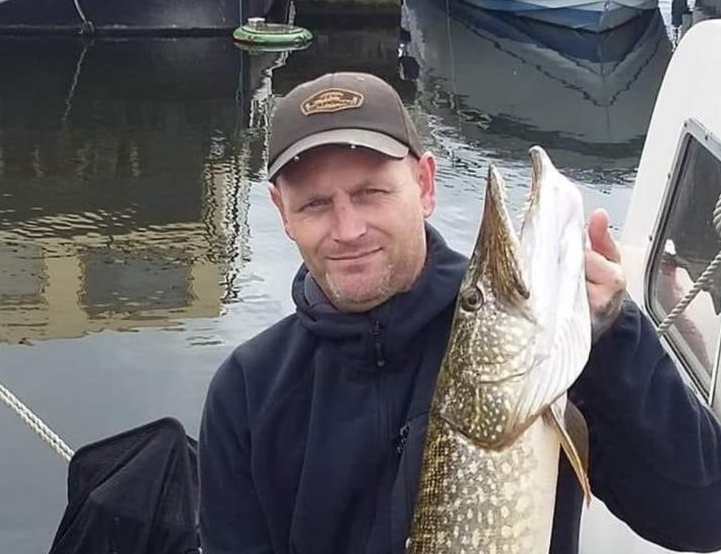Ian Morley holding a fish and wearing a baseball cap