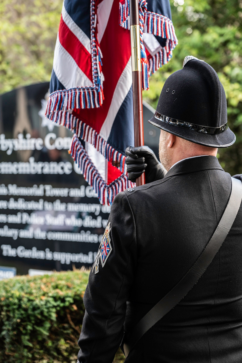 A police officer holds a flag in front of the sign for the Remembrance garden