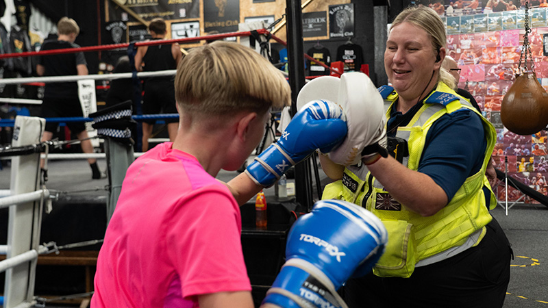 A PCSO holds boxing pads as a young person hits them with boxing gloves on.