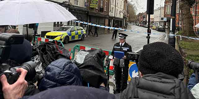 Officer stands before press delivering an update. The press are in the foreground and it is raining. 